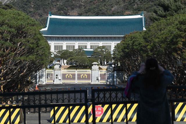 A woman takes pictures in front of the Blue House, known as Cheong Wa Dae in Korean, in Seoul on December 22, 2025. South Korea's president and his team have started moving back into Seoul's historic Blue House and the process will be wrapped up by Christmas, an official said on December 9. (Photo by Jung Yeon-je / AFP)