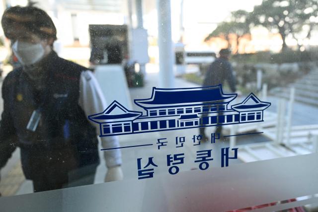 Workers carrying belongings are seen through a glass door at the Presidential Office in Seoul on December 22, 2025, as South Korea's presidential office is moved back to the Blue House. South Korea's president and his team have started moving back into Seoul's historic Blue House and the process will be wrapped up by Christmas, an official said on December 9. (Photo by Jung Yeon-je / AFP)