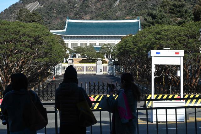 Tourists take pictures in front of the Blue House, known as Cheong Wa Dae in Korean, in Seoul on December 22, 2025. South Korea's president and his team have started moving back into Seoul's historic Blue House and the process will be wrapped up by Christmas, an official said on December 9. (Photo by Jung Yeon-je / AFP)