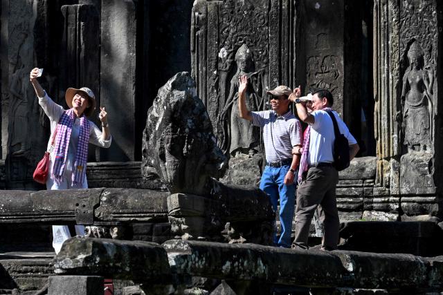 This photo taken on December 18, 2025 shows tourists taking selfie photos as they visit the Bayon temple in Siem Reap province.  (Photo by TANG CHHIN Sothy / AFP)