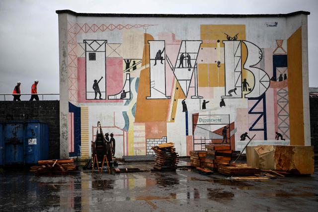 This photograph shows a wall covered with a fresco depicting construction activities through the letters LMB at the Lycee des Metiers du Batiment (LMB - Building Trades High School), which provides instruction to high school students and over 100 university students in the construction and architecture fields in Felletin on December 10, 2025. Weight room, athletics track, football stadium, indoor swimming pool, cinema: the list of facilities at this institution specialised in construction trades is reminiscent of an American campus... (Photo by Christophe ARCHAMBAULT / AFP)