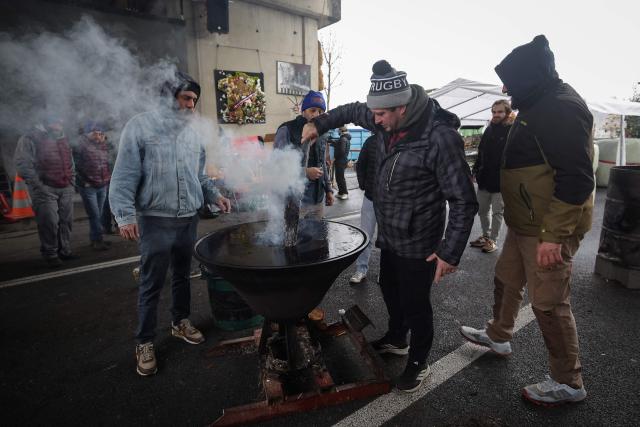 Farmers fuel the fire as they gather on the A64 motorway during a farmers blockade to protest against the government's mandatory culling protocol for cattle herds affected by lumpy skin disease (dermatose nodulaire contagieuse), in Carbonne south-western France, on December 22, 2025. (Photo by Valentine CHAPUIS / AFP)