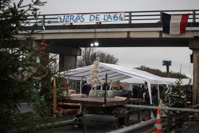 A banner reading "The A64 ultras" is hung above the highway during a farmers blockade to protest against the government's mandatory culling protocol for cattle herds affected by lumpy skin disease (dermatose nodulaire contagieuse), in Carbonne, south-western France on December 22, 2025. (Photo by Valentine CHAPUIS / AFP)