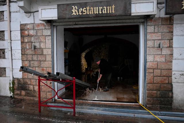 A man cleans up water inside a restaurant after the Herault river flooded following heavy rains in Laroque, southern France, on December 22, 2025. From Tarn to Var, five departments in the south of the country have been placed on orange alert on December 22, 2025 by Meteo-France for flooding or heavy rain. Aveyron and Tarn are also on orange alert for snow and ice. (Photo by Sylvain THOMAS / AFP)