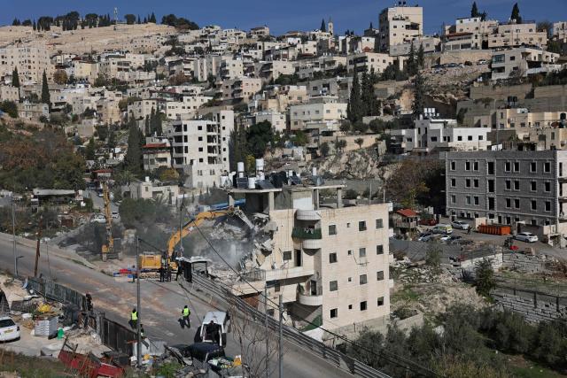 Israeli forces gather as an excavator demolishes a building constructed without a permit in the Wadi Qaddum area near the Silwan neighbourhood of east Jerusalem on December 22, 2025. Israeli bulldozers tore through a four-storey residential building in east Jerusalem on December 22, displacing scores of Palestinians in what activists said was the largest such demolition in the area this year. (Photo by AHMAD GHARABLI / AFP)