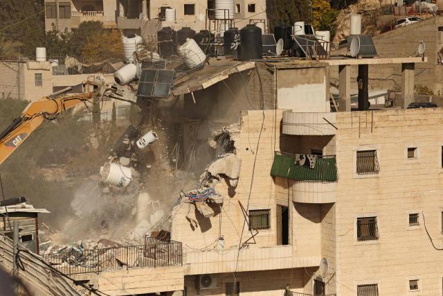 An excavator demolishes a building constructed without a permit in the Wadi Qaddum area near the Silwan neighbourhood of east Jerusalem on December 22, 2025. Israeli bulldozers tore through a four-storey residential building in east Jerusalem on December 22, displacing scores of Palestinians in what activists said was the largest such demolition in the area this year. (Photo by AHMAD GHARABLI / AFP)