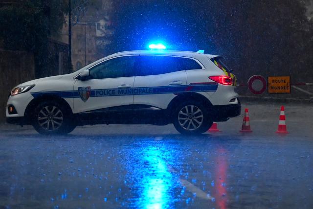 A police car is parked in front of a road sign reading "flooded road" on the banks of the Herault river which overflowed following heavy rains in Laroque, southern France, on December 22, 2025. From Tarn to Var, five departments in the south of the country have been placed on orange alert on December 22, 2025 by Meteo-France for flooding or heavy rain. Aveyron and Tarn are also on orange alert for snow and ice. (Photo by Sylvain THOMAS / AFP)