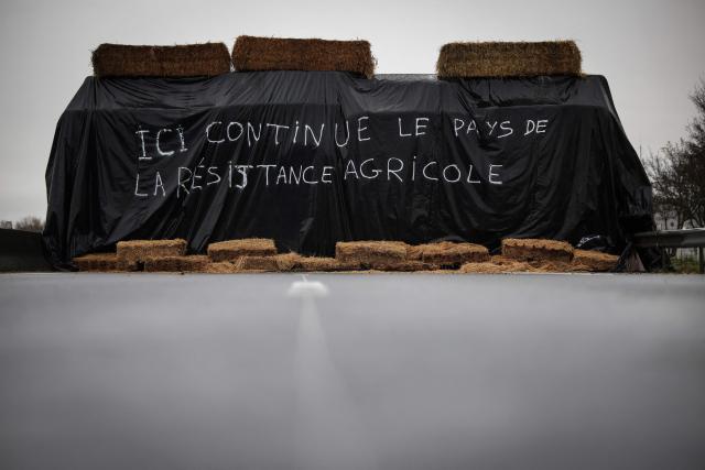 A straw wall bearing the inscription "Here continues the land of agricultural resistance" is seen on the A64 motorway, while farmers continue to block the motorway to protest against the government's mandatory culling protocol for cattle herds affected by lumpy skin disease (dermatose nodulaire contagieuse), in Carbonne, south-western France on December 22, 2025. (Photo by Valentine CHAPUIS / AFP)