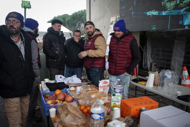French agricultural activist Jerome Bayle (2nd R) stands with farmers as they continue to block the motorway to protest against the government's mandatory culling protocol for cattle herds affected by lumpy skin disease (dermatose nodulaire contagieuse), in Carbonne, south-western France on December 22, 2025. (Photo by Valentine CHAPUIS / AFP)
