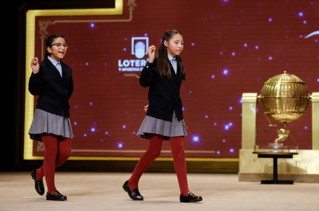 Schoolgirls show the winning prize of Spain's Christmas lottery "El Gordo" (the Fat One) at the Royal Theatre in Madrid on December 22, 2025. (Photo by OSCAR DEL POZO / AFP)