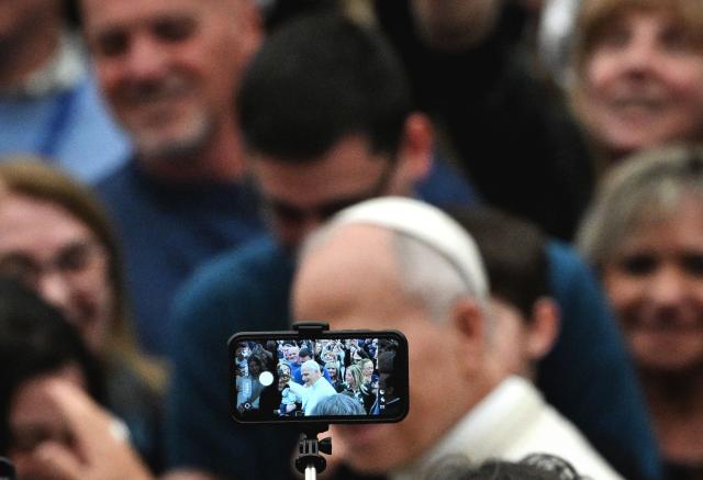 A man takes a photo as Pope Leo XIV leaves at the end of an audience in the Paul VI Hall in the Vatican on December 22, 2025, for Christmas greetings to the employees of the Holy See, the Governorate of Vatican City State and the Vicariate of Rome. (Photo by TIZIANA FABI / AFP)