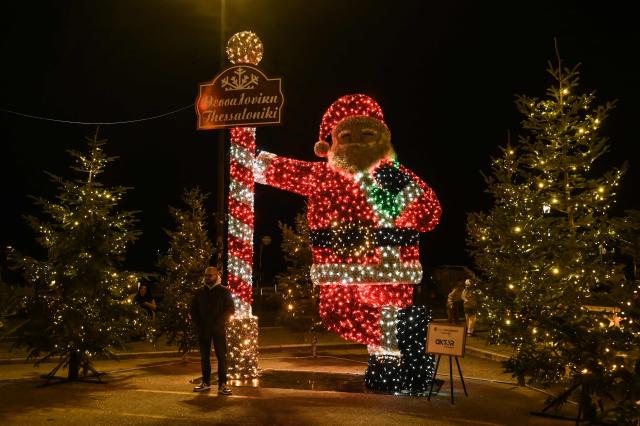 A man poses for pictures next to a giant illuminated Father Christmas in Thessaloniki, on December 22, 2025. (Photo by Sakis Mitrolidis / AFP)