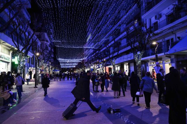 Pedestrians walk down a street illuminated by Festive decorations in Thessaloniki, on December 22, 2025. (Photo by Sakis Mitrolidis / AFP)