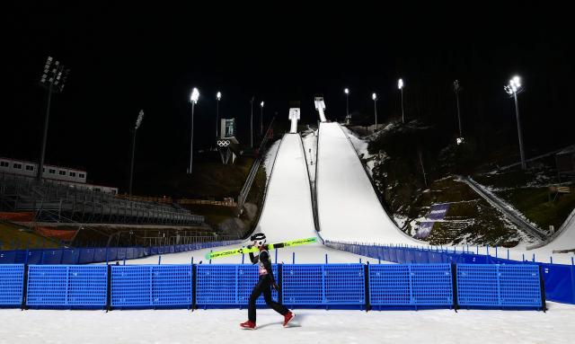 An athlete carries his ski as he walks during a training session at the Ski Jumping arena prior the Open Italian Championship of ski jumping in Predazzo, on December 22, 2025. The Ski Jumping arena in Predazzo will host the ski jumping and nordic combined competitions, during the Milano Cortina 2026 Winter Olympic Games. (Photo by Stefano RELLANDINI / AFP)