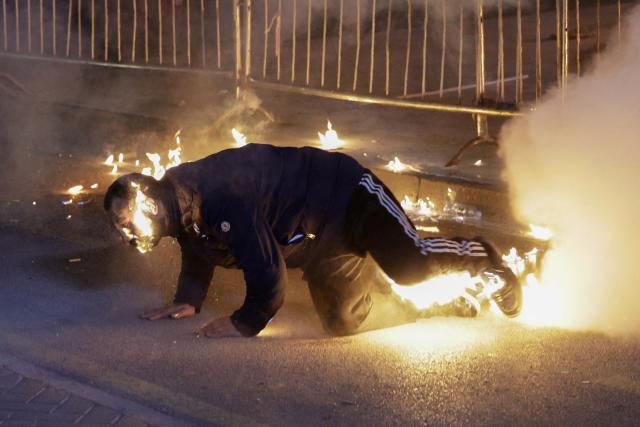 An opposition supporter tries to extinguish fire on his body after a molotov cocktail was mistakenly thrown on him during a protest in front of the Prime Minister's office in Tirana on December 22, 2025. Major opposition parties are calling for the government to resign, after allegations have been levelled against Belinda Balluku, Albania’s deputy prime minister and minister for infrastructure and energy. (Photo by Adnan Beci / AFP)