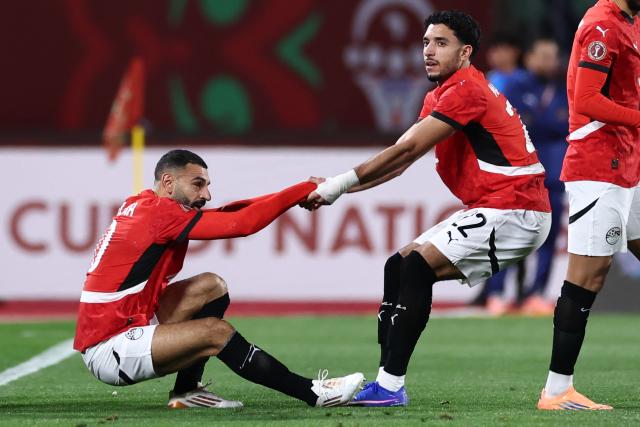 Egypt's forward #10 Mohamed Salah is helped by Egypt's forward #22 Omar Marmoushra during the Africa Cup of Nations (CAN) group B football match between Egypt and Zimbabwe at Adrar Stadium in Agadir on December 22, 2025. (Photo by FRANCK FIFE / AFP)