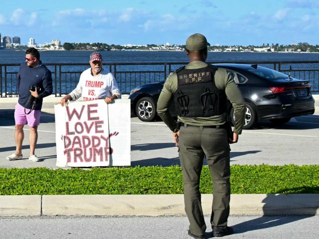 A supporter holds a "We Love 'Daddy' Trump" sign as US President Donald Trum'’s motorcade passes while returning to his Mar-a-Lago club in Palm Beach, Florida, on December 22, 2025. (Photo by ANDREW CABALLERO-REYNOLDS / AFP)
