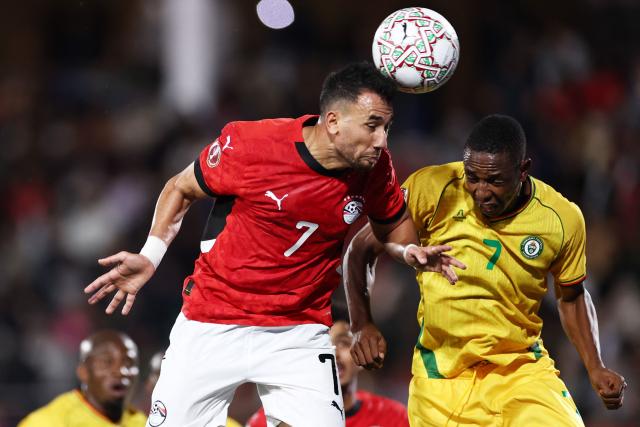 Egypt's forward #7 Mahmoud Trezeguet (L) and Zimbabwe's forward #07 Prince Dube jump for the ball during the Africa Cup of Nations (CAN) group B football match between Egypt and Zimbabwe at Adrar Stadium in Agadir on December 22, 2025. (Photo by FRANCK FIFE / AFP)