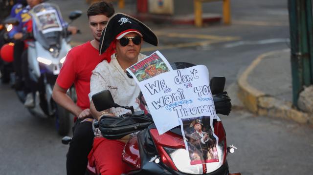 A motorcyclist with images of US President Donald Trump dressed as a pirate attached to his bike takes part in a motorcade to protest against the United States in Caracas on December 22, 2025. Dressed as pirates, dozens of motorcyclists rode through Caracas on December 22 to protest the seizure of ships carrying Venezuelan oil by the United States as part of its blockade against sanctioned tankers. (Photo by Pedro MATTEY / AFP)