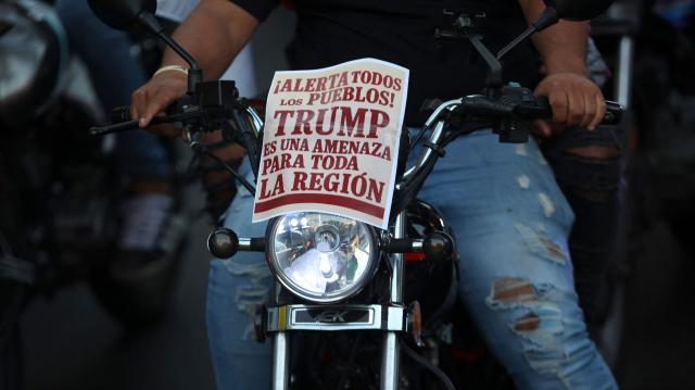 A motorcyclist with a sign reading "Alert all peoples, Trump is a threat to the entire region" attached to his bike takes part in a motorcade to protest against the United States in Caracas on December 22, 2025. Dressed as pirates, dozens of motorcyclists rode through Caracas on December 22 to protest the seizure of ships carrying Venezuelan oil by the United States as part of its blockade against sanctioned tankers. (Photo by Pedro MATTEY / AFP)