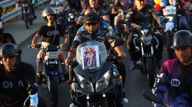 A motorcyclist with an image of US President Donald Trump dressed as a pirate attached to his bike takes part in a motorcade to protest against the United States in Caracas on December 22, 2025. Dressed as pirates, dozens of motorcyclists rode through Caracas on December 22 to protest the seizure of ships carrying Venezuelan oil by the United States as part of its blockade against sanctioned tankers. (Photo by Pedro MATTEY / AFP)