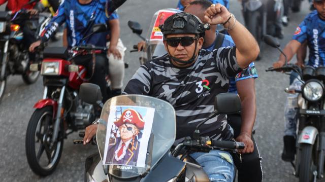 A motorcyclist with an image of US President Donald Trump dressed as a pirate attached to his bike takes part in a motorcade to protest against the United States in Caracas on December 22, 2025. Dressed as pirates, dozens of motorcyclists rode through Caracas on December 22 to protest the seizure of ships carrying Venezuelan oil by the United States as part of its blockade against sanctioned tankers. (Photo by Pedro MATTEY / AFP)