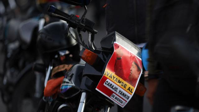 A motorcyclist with a photo of late Venezuelan President Hugo Chavez and a sign reading "Go to hell, damn Yankees" attached to his bike takes part in a motorcade to protest against the United States in Caracas on December 22, 2025. Dressed as pirates, dozens of motorcyclists rode through Caracas on December 22 to protest the seizure of ships carrying Venezuelan oil by the United States as part of its blockade against sanctioned tankers. (Photo by Pedro MATTEY / AFP)