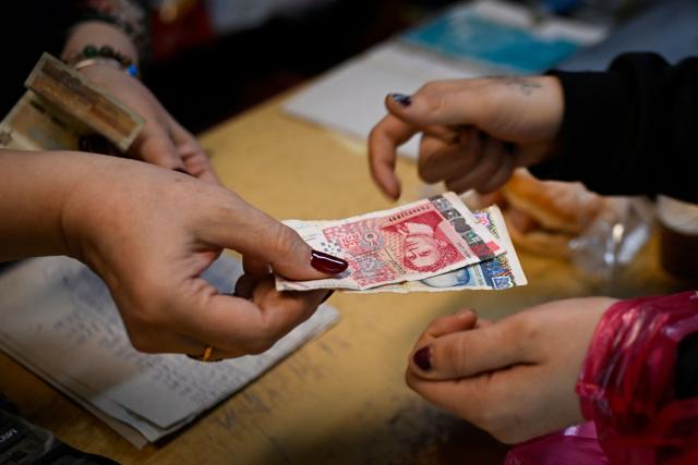 A grocery store owner returns lev banknotes to a customer in a grocery store in the village of Chuprene, northwestern Bulgaria on December 7, 2025. Bulgaria shaken by political uncertainty, with the latest short-lived government resigning last week -- becomes the single currency area's 21st member on January 1, nearly 19 years after the country of 6.4 million people joined the European Union. (Photo by Nikolay DOYCHINOV / AFP)
