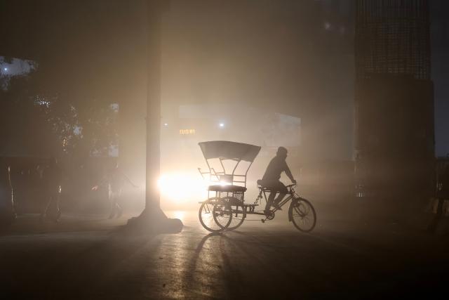 A rickshaw puller pedals along a road amid dense smog during a winter morning in Varanasi on December 23, 2025. (Photo by Niharika KULKARNI / AFP)
