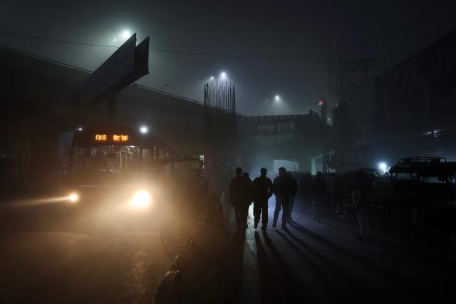 People walk along a road amid dense smog during a winter morning in Varanasi on December 23, 2025. (Photo by Niharika KULKARNI / AFP)