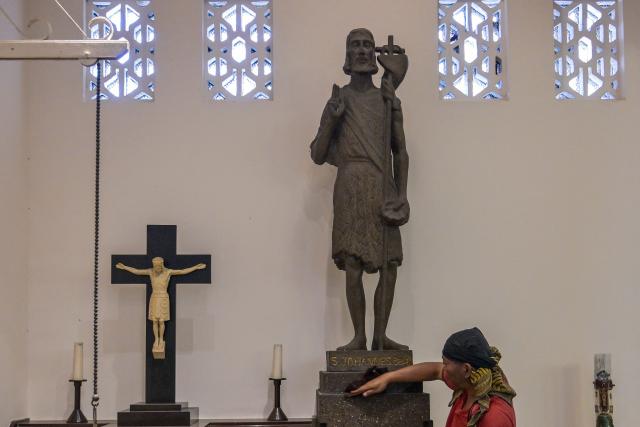 A worker cleans a statue of Saint John the Baptist at the Sacred Heart of Jesus Cathedral, known locally as the "Hati Kudus Yesus" church, during preparations for Christmas Mass in Surabaya, Indonesia's East Java province on December 23, 2025. (Photo by JUNI KRISWANTO / AFP)
