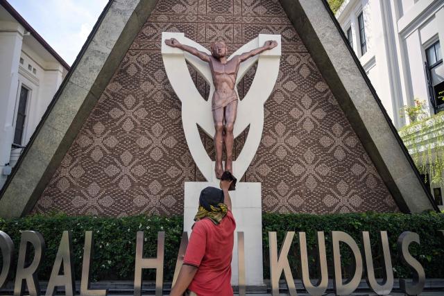 A worker cleans a statue of Jesus at the Sacred Heart of Jesus Cathedral, known locally as the "Hati Kudus Yesus" church, during preparations for Christmas Mass in Surabaya, Indonesia's East Java province on December 23, 2025. (Photo by JUNI KRISWANTO / AFP)