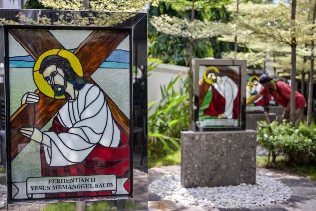 A worker cleans a portrait of Jesus at the Sacred Heart of Jesus Cathedral, known locally as the "Hati Kudus Yesus" church, during preparations for Christmas Mass in Surabaya, Indonesia's East Java province on December 23, 2025. (Photo by JUNI KRISWANTO / AFP)