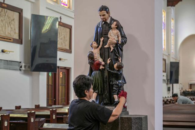 A worker cleans a statue of Saint Vincent de Paul at the Sacred Heart of Jesus Cathedral, known locally as the "Hati Kudus Yesus" church, during preparations for Christmas Mass in Surabaya, Indonesia's East Java province on December 23, 2025. (Photo by JUNI KRISWANTO / AFP)