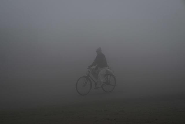 A cyclist rides along a street engulfed in dense smog in Lahore on December 23, 2025. (Photo by Arif ALI / AFP)