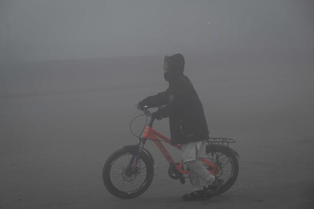 A boy pushes his bicycle along a street amid dense smog in Lahore on December 23, 2025. (Photo by Arif ALI / AFP)