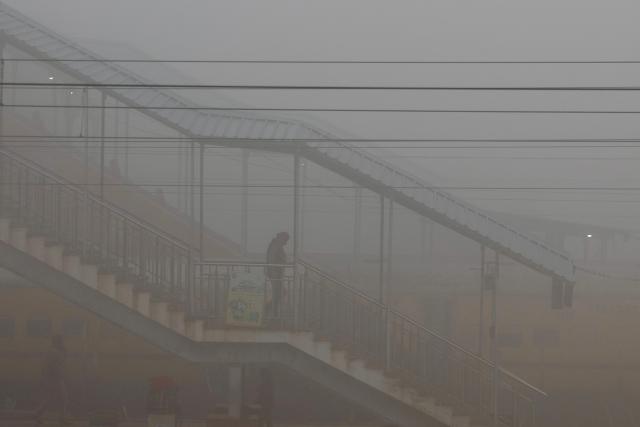 A passenger walks on a bridge connecting platforms at a railway station amid dense smog during a winter morning in Varanasi on December 23, 2025. (Photo by Niharika KULKARNI / AFP)