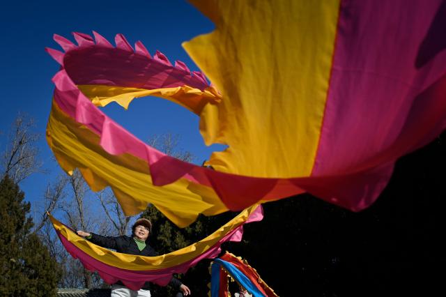 A woman dances with ribbons at a park in Beijing on December 23, 2025. (Photo by WANG Zhao / AFP)