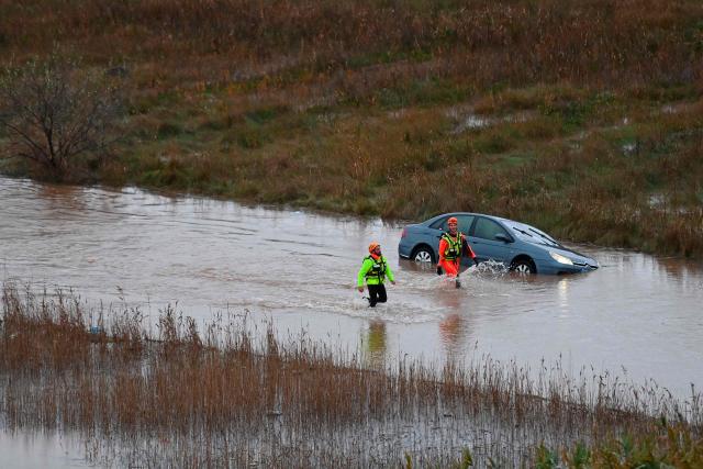 French rescue workers walk past a car along the Herault river which overflowed following heavy rains in Agde, southern France on December 23, 2025. The Herault department remains under red alert on December 23, 2025, for exceptional flooding, which occurred the previous day following heavy rainfall that is moving away, according to France's weather agency Meteo-France, while the departments of Tarn, Aveyron and Lozere are placed on orange alert for risk of flooding. (Photo by Sylvain THOMAS / AFP)