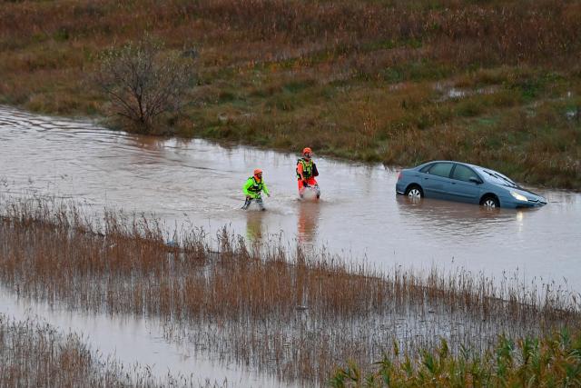 French rescue workers walk past a car along the Herault river which overflowed following heavy rains in Agde, southern France on December 23, 2025. The Herault department remains under red alert on December 23, 2025, for exceptional flooding, which occurred the previous day following heavy rainfall that is moving away, according to France's weather agency Meteo-France, while the departments of Tarn, Aveyron and Lozere are placed on orange alert for risk of flooding. (Photo by Sylvain THOMAS / AFP)