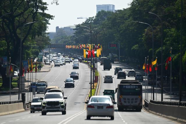 Vehicles drive on a road with the national flags displayed ahead of Myanmar's general election in Yangon on December 23, 2025. Myanmar junta has touted polls starting December 28 as a path to peace, but the vote will be blocked from rebel-held enclaves and monitors are dismissing it as a ploy to disguise continuing military rule. (Photo by Sai Aung MAIN / AFP)