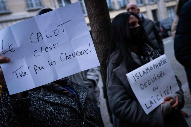 People hold signs to show support to nurse Majdouline who was dismissed from the civil service for wearing a skullcap speaks to journalists in front of the administrative court in Paris on December 23, 2025. (Photo by BERTRAND GUAY / AFP)