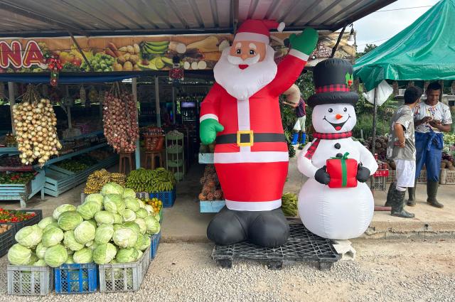 Two workers talk next to inflatable Christmas decorations at a greengrocer's in Havana on December 23, 2025. (Photo by YAMIL LAGE / AFP)