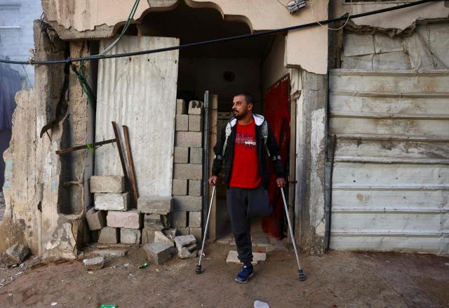 Bassam Omar Shaheen, 37, stands outside his home in Gaza City's Al-Saftawi neighbourhood in the northern Gaza Strip on December 23, 2025. Omar was injured in an attack on a school on November 3, 2023 in the Al-Saftawi neighbourhood in the northern Gaza Strip, in which his father and mother were killed, and his leg was amputated as a result. He has been waiting for two years to travel to complete treatment for his hand, which requires surgery due to damage to his fingers and palm. The war was sparked by Hamas's October 7, 2023 attack on Israel, which resulted in the deaths of 1,221 people. Israel's retaliatory assault on Gaza has killed over 70,000 people, according to figures from the health ministry that the UN considers reliable. (Photo by Bashar Taleb / AFP)