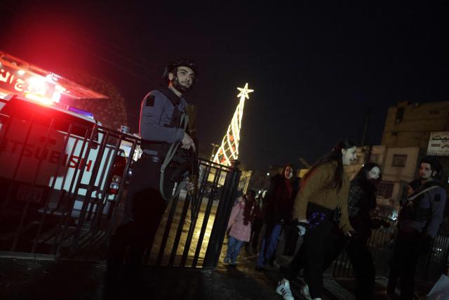 A member of the security forces stands guard as people walk following increased security measures at Damascus Christian sites and areas ahead of Christmas on December 23, 2025. In early December, the Syrian president urged Syrians to work together to rebuild the country as they marked a year since the ousting of longtime ruler Bashar al-Assad. (Photo by Bakr ALKASEM / AFP)