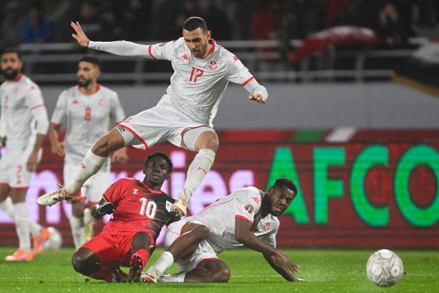 TOPSHOT - Tunisia's midfielder #17 Ellyes Skhiri jumps over Uganda's midfielder #10 Travis Mutyaba and Tunisia's forward #19 Firas Chaouat during the Africa Cup of Nations (CAN) Group C football match between Tunisia and Uganda at Rabat Olympic Stadium in Rabat on December 23, 2025. (Photo by SEBASTIEN BOZON / AFP)