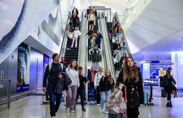 Passengers go down the escalators after arriving to La Guardia Airport on December 23, 2025 in New York. (Photo by kena betancur / AFP)
