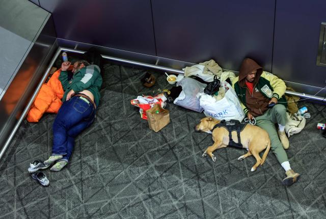 Travelers rest on a lounge of La Guardia Airport on December 23, 2025 in New York. (Photo by kena betancur / AFP)