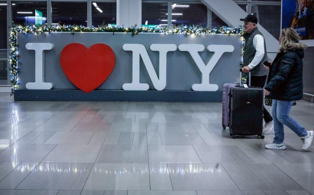 A couple of travelers walk through the arrival hall after arriving to La Guardia Airport on December 23, 2025 in New York. (Photo by kena betancur / AFP)