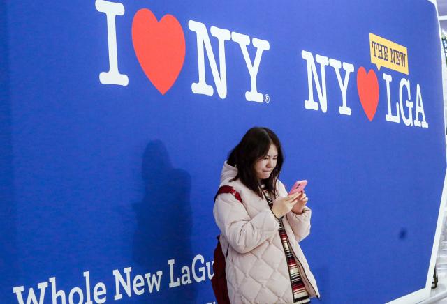 A woman checks her phone in the check-in area of La Guardia Airport on December 23, 2025 in New York. (Photo by kena betancur / AFP)